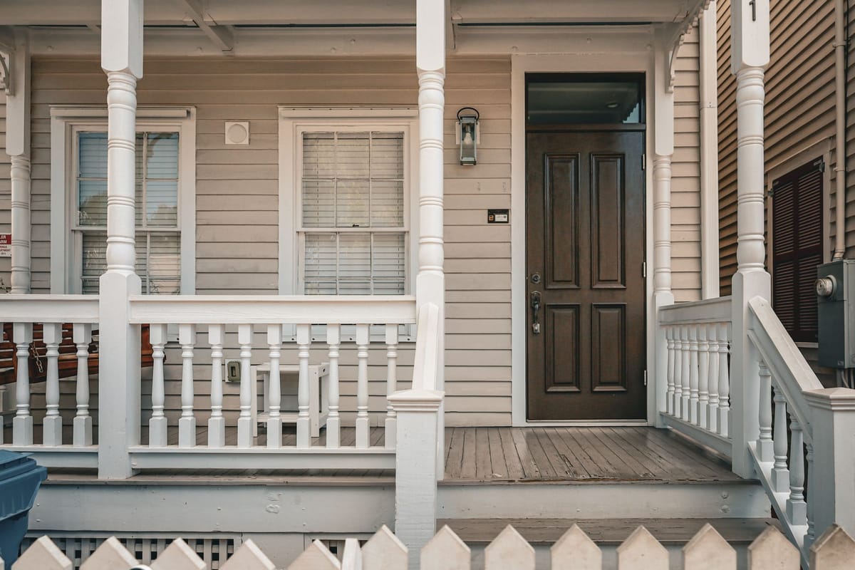 Front porch of a traditional American home with white railings and a dark wood front door, typical of homes for sale by owner.