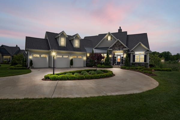Elegant suburban home for sale at dusk with circular driveway and glowing exterior lights.